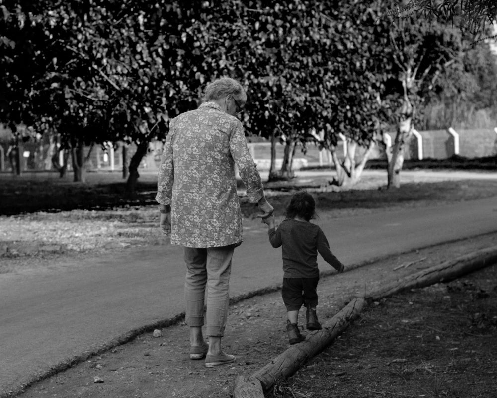 Black and white photo of an older person and a child walking together on a path.