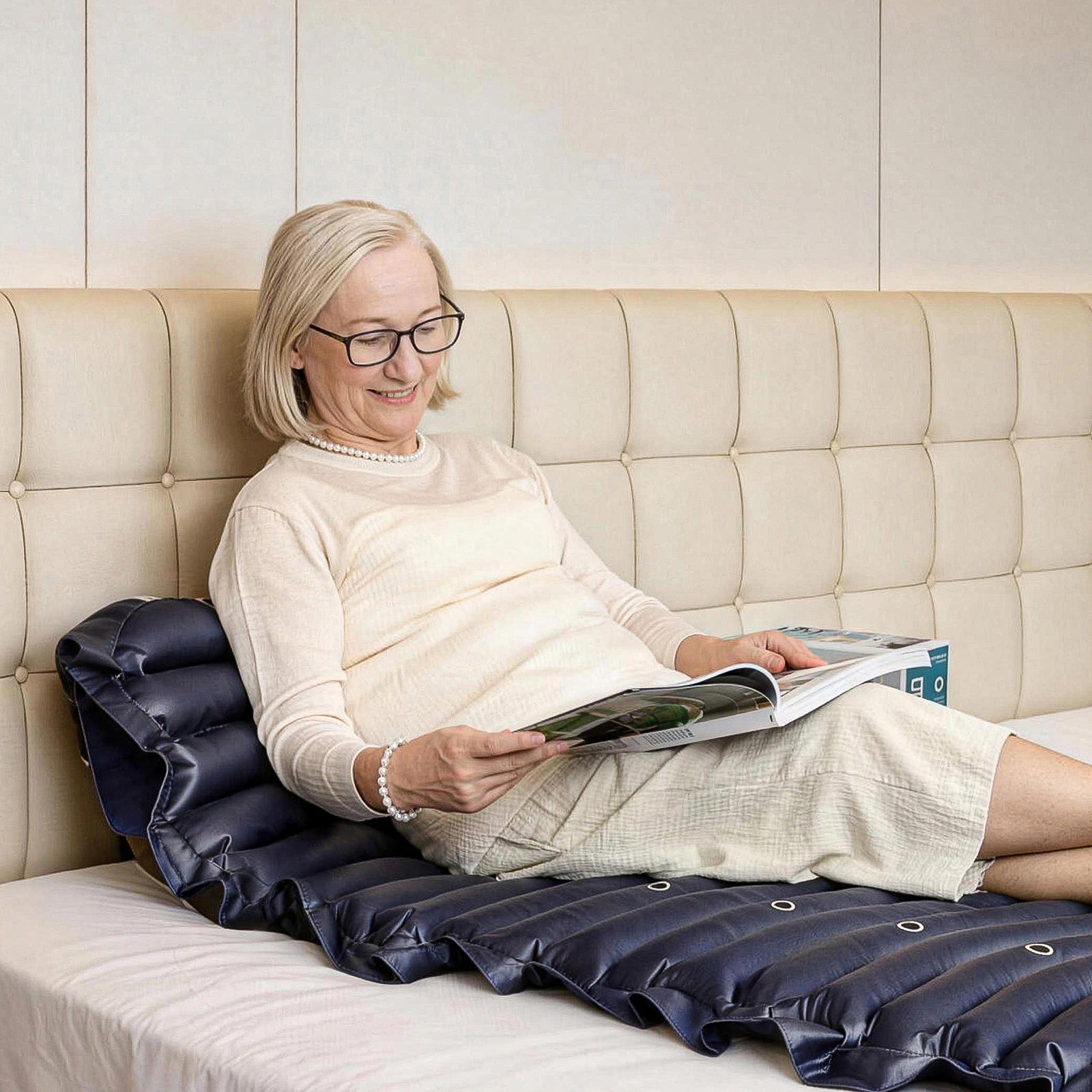 Woman sitting on a beige couch with a kekoy air mattress, reading a magazine.