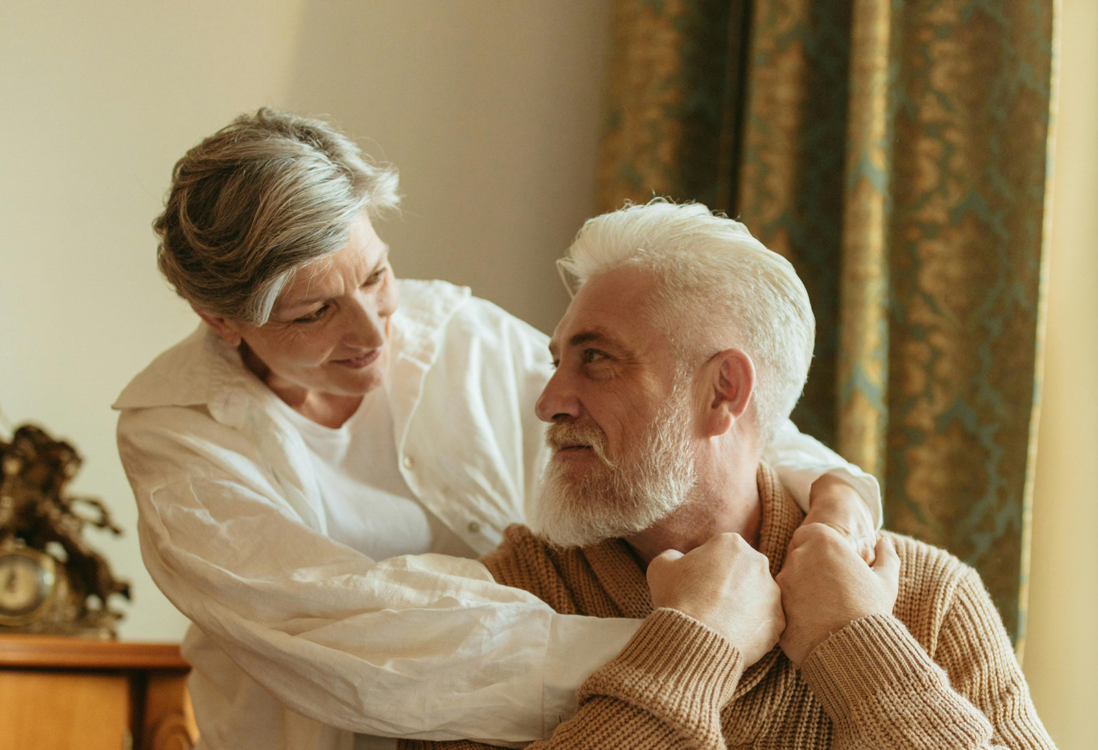 Two elderly people embracing each other in a warm indoor setting.