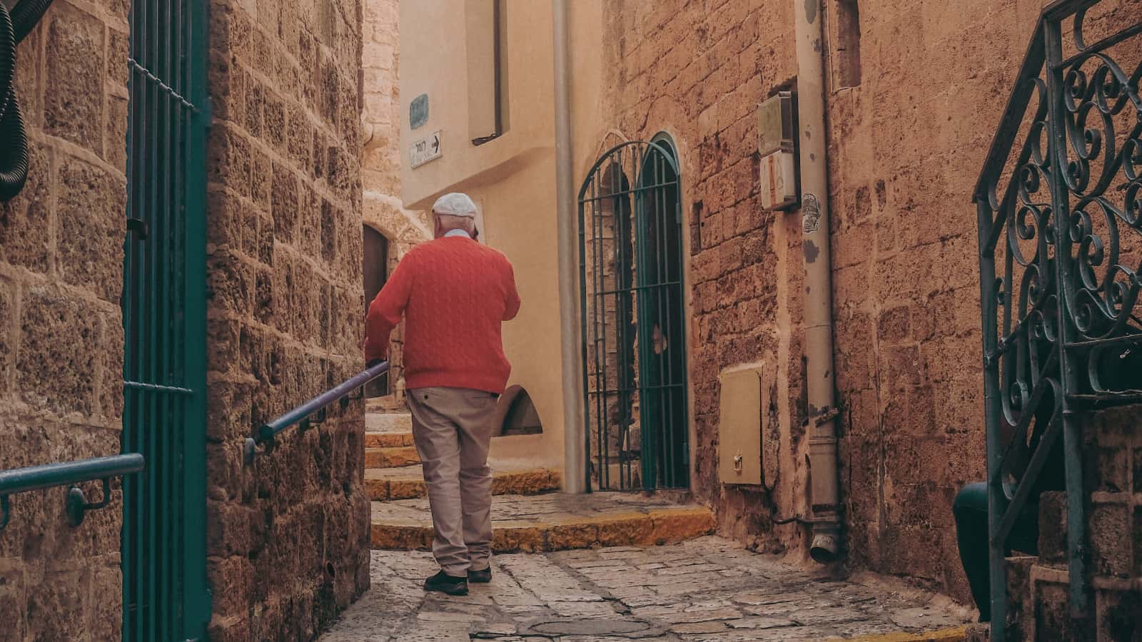 elder in red walks down stone alleyway